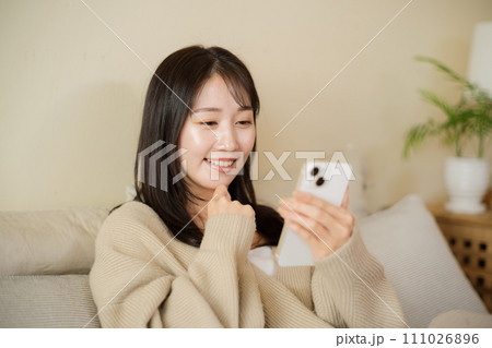部屋のベッドでスマホを見る女性 111026896