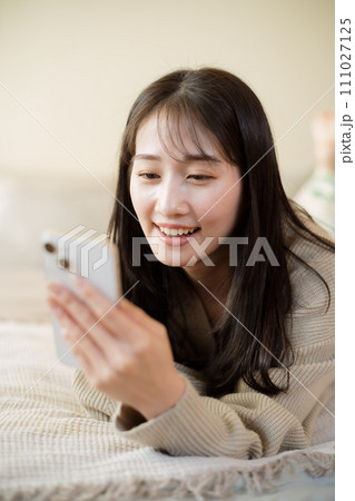 ベッドの上でスマートフォンを触る女性 111027125