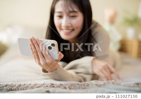 ベッドの上でスマートフォンを触る女性 111027130