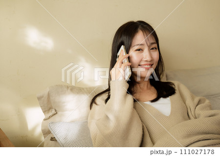 ベッドの上でスマートフォンを触る女性 ベッドの上でスマートフォンを触る女性 111027178