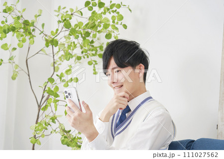 リビングで考えながらスマートフォンでを使う男子高校生 リビングで考えながらスマートフォンでを使う男子高校生 111027562