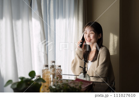 窓際で携帯電話を使って通話をする女性 111027610