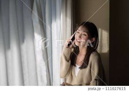 窓際で携帯電話を使って通話をする女性 111027615