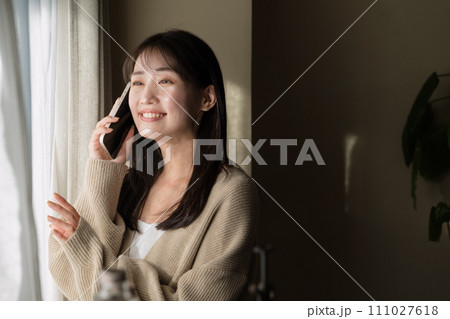 窓際で携帯電話を使って通話をする女性 111027618