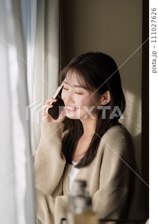 窓際で携帯電話を使って通話をする女性 111027626
