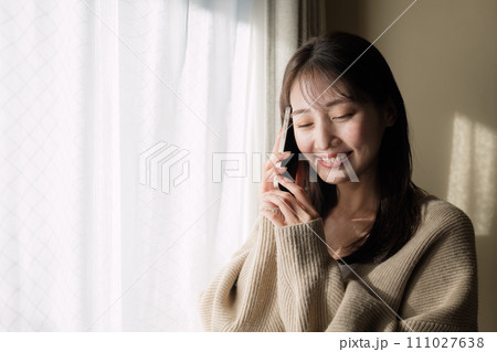窓際で携帯電話を使って通話をする女性 111027638