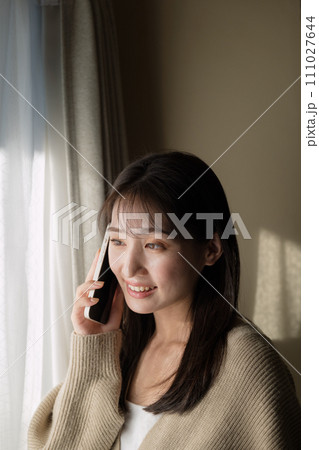 窓際で携帯電話を使って通話をする女性 窓際で携帯電話を使って通話をする女性 111027644