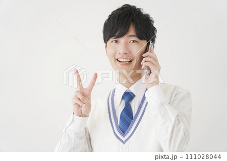 スマートフォンで電話しながらピースサインをする男子高校生 白背景 スマートフォンで電話しながらピースサインをする男子高校生 白背景 111028044