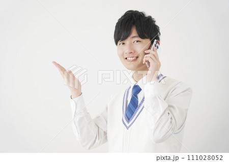 スマートフォンで電話しながら手のひらで左側を指す男子高校生 白背景 スマートフォンで電話しながら手のひらで左側を指す男子高校生 白背景 111028052