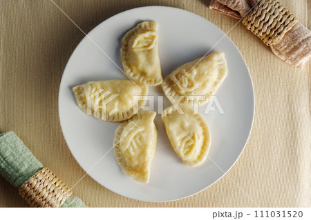 Elegance of perfectly crimped crescent dumplings, or ravioli, presented on a white plate, ready to entice any food connoisseur. 111031520