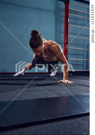 Young man with sportive, muscular, strong body training shirtless, doing one arm push ups in gym Young man with sportive, muscular, strong body training shirtless, doing one arm push ups in gym 111031834