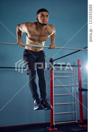 Following heathy routine. Muscular athletic young man with sportive fit body training shirtless, doing pull ups exercises in gym 111031888