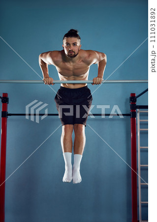 Following heathy routine. Muscular athletic young man with sportive fit body training shirtless, doing pull ups exercises in gym Following heathy routine. Muscular athletic young man with sportive fit body training shirtless, doing pull ups exercises in gym 111031892