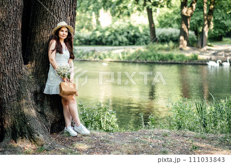 Eco-Friendly Lifestyle. Woman in Nature with Sustainable Fashion Choices. Outdoors woman embodying eco-friendly lifestyle with straw hat, dress, and basket, holding a bouquet of wildflowers. Eco-Friendly Lifestyle. Woman in Nature with Sustainable Fashion Choices. Outdoors woman embodying eco-friendly lifestyle with straw hat, dress, and basket, holding a bouquet of wildflowers. 111033843