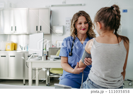 Doctor examining young girl, measuring blood pressure, using medical blood pressure monitor. Concept of preventive health care for children. Doctor examining young girl, measuring blood pressure, using medical blood pressure monitor. Concept of preventive health care for children. 111035858