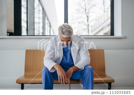 Frustrated, exhausted doctor sitting on bench in hospital corridor. Concept of burnout syndrome among doctors. 111035885