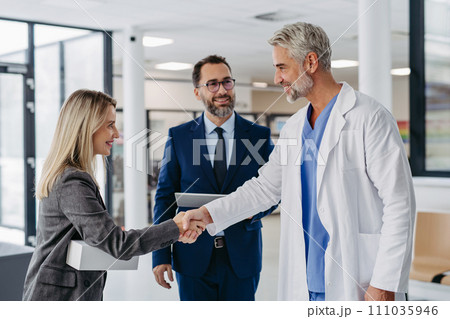 Pharmaceutical sales representatives meeting doctor in medical building, shaking hands. Hospital director and manager talking with head physician in modern clinic, hospital. Pharmaceutical sales representatives meeting doctor in medical building, shaking hands. Hospital director and manager talking with head physician in modern clinic, hospital. 111035946