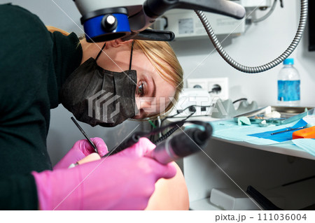 Close-up of female dentist who is learning to treat teeth on human head mannequin. Medical student in protective mask and sterile gloves holding a dental drill. Stomatology and orthodontics concept. Close-up of female dentist who is learning to treat teeth on human head mannequin. Medical student in protective mask and sterile gloves holding a dental drill. Stomatology and orthodontics concept. 111036004
