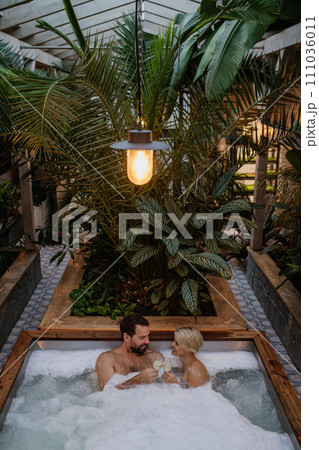 Beautiful mature couple relaxing in hot tub, drinking champagne, enjoying romantic wellness weekend in spa. Concept of Valentine's Day. Beautiful mature couple relaxing in hot tub, drinking champagne, enjoying romantic wellness weekend in spa. Concept of Valentine's Day. 111036011