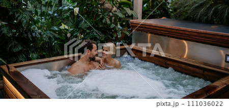 Beautiful mature couple relaxing in hot tub, enjoying romantic wellness weekend in spa. Concept of Valentine's Day. Banner with copy space. 111036022