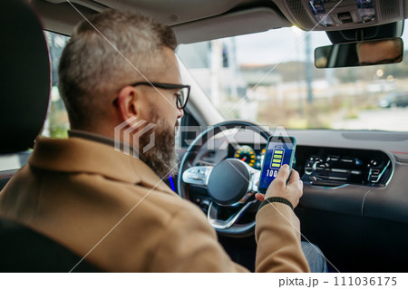 Close up of man using electric vehicle charging app, checking battery level on smart phone. Charging apps for monitoring electricity usage, locating charging stations. 111036175