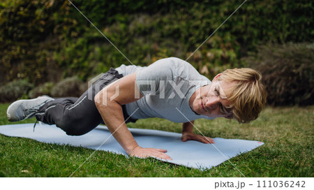 Middle aged man exercising outdoors in garden, doing push ups.. Concept of workout routine at home. 111036242