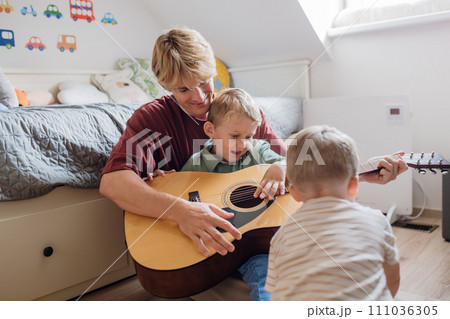 Father teaching boy to play on guitar. Son having fun in their room with dad, playing guitar and singing together. Concept of Father's Day, and fatherly love. 111036305