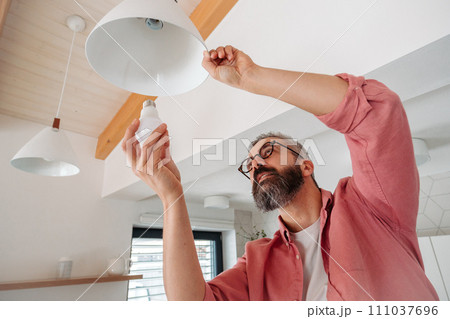 Man changing LED bulbs at home. Concept of energy efficiency, longevitiy and environmental impact of electronic bulb. 111037696
