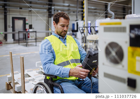 Portrait of man in wheelchair working in modern industrial factory, scanning with scanner. Concept of workers with disabilities, accessible workplace for employees with mobility impairment. 111037726