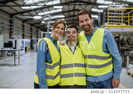 Portrait of young man with Down syndrome and his colleagues working in warehouse, holding around shoulders. Concept of workers with disabilities, support in workplace. Portrait of young man with Down syndrome and his colleagues working in warehouse, holding around shoulders. Concept of workers with disabilities, support in workplace. 111037731