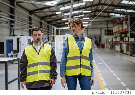 Young man with Down syndrome working in warehouse, colleague talking with him. Concept of workers with disabilities, support in workplace. Young man with Down syndrome working in warehouse, colleague talking with him. Concept of workers with disabilities, support in workplace. 111037732