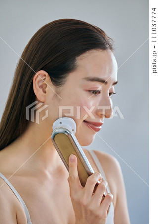 美顔器を使ってスキンケアをするロングヘアの30代女性 111037774