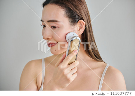 美顔器を使ってスキンケアをするロングヘアの30代女性 美顔器を使ってスキンケアをするロングヘアの30代女性 111037777