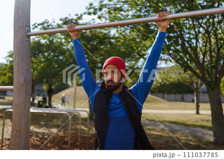 Handsome man exercises outdoors at an urban outdoor gym. Exercising after work for good mental health, physical health, and relieving stress and boost mood. 111037785