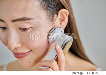美顔器を使ってスキンケアをするロングヘアの30代女性 111038356