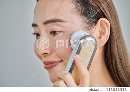 美顔器を使ってスキンケアをするロングヘアの30代女性 111038358