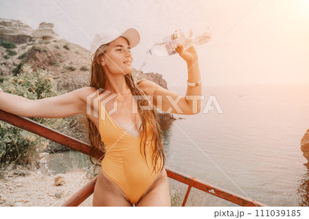 Woman travel sea. Happy tourist enjoy taking picture outdoors for memories. Woman traveler drinks water at the edge of the cliff on the sea bay of mountains, sharing travel adventure journey Woman travel sea. Happy tourist enjoy taking picture outdoors for memories. Woman traveler drinks water at the edge of the cliff on the sea bay of mountains, sharing travel adventure journey 111039185