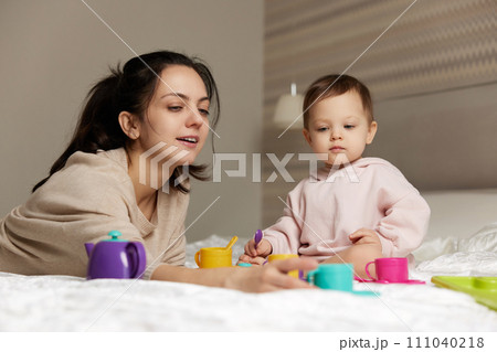 mother and little child daughter playing tea party and spending time together in bedroom, family having fun, 111040218