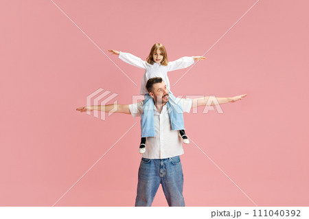 Father and daughter with arms outstretched, play airplanes pretending to fly against pink pastel background. Concept of International Day of Happiness 111040392