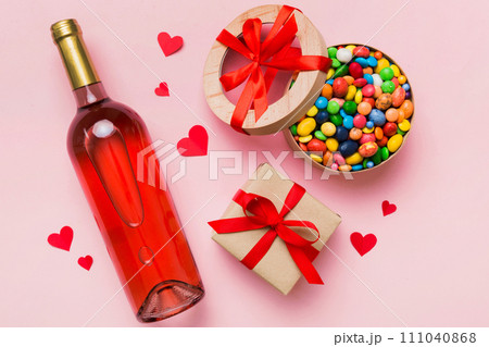 Bottle of red wine on colored background for Valentine Day with gift and chocolate. Heart shaped with gift box of chocolates top view with copy space Bottle of red wine on colored background for Valentine Day with gift and chocolate. Heart shaped with gift box of chocolates top view with copy space 111040868