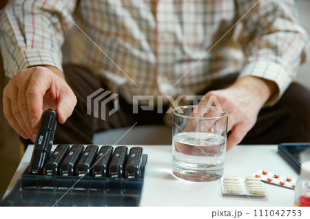 Hands of a senior man holding pill box, medication containers labeled with days of week. Organizer for daily pills and vitamins 111042753