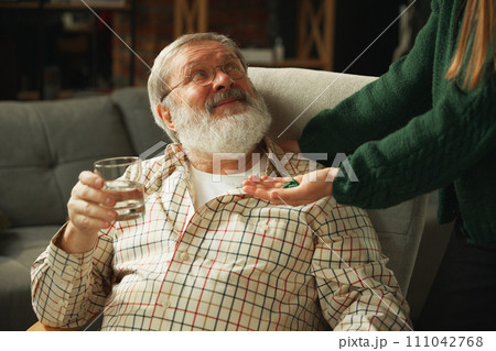 Heart pains. Elderly man in glasses holding water, getting pill from hand. Support and care of relatives 111042768