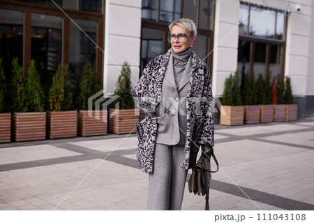 Stylish blonde mature woman with short hair wears fashionable winter multilayer outfit, animal print coat, grey wool suit with turtleneck and eyeglasses, stands in city. Elder Female in Trendy clothes Stylish blonde mature woman with short hair wears fashionable winter multilayer outfit, animal print coat, grey wool suit with turtleneck and eyeglasses, stands in city. Elder Female in Trendy clothes 111043108