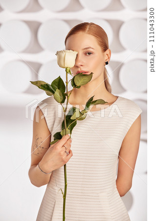 Portrait of a beautiful young disabled woman, born without an arm, holding a flower in her hands in a white dress. Diversity disability and flowers. 111043300