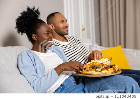 Man and woman family enjoying movie on weekend eating pizza and popcorn while sitting on couch Man and woman family enjoying movie on weekend eating pizza and popcorn while sitting on couch 111043409