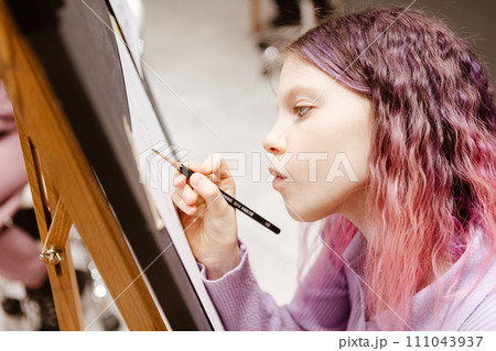 Girl 11 years old craftswoman are painting on canvas in studio standing in front of easel. Portrait of a girl painting during an art class. 111043937