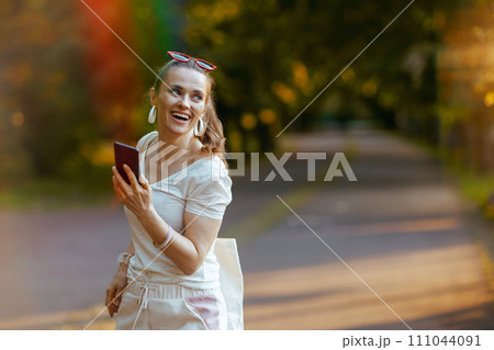 smiling stylish woman in white shirt with smartphone walking smiling stylish woman in white shirt with smartphone walking 111044091