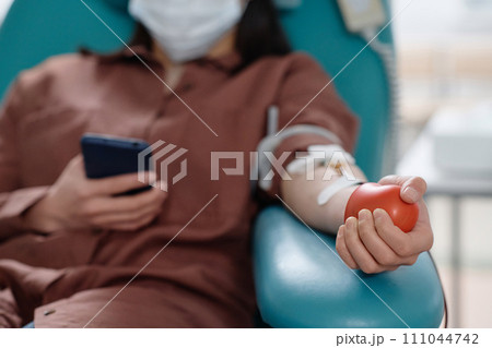 Hand of blood donor in protective mask squeezing red rubber ball during transfusion process Hand of blood donor in protective mask squeezing red rubber ball during transfusion process 111044742
