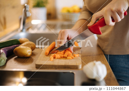 Close-up of female using knife and cutting carrot on wooden table. Home food concept  111044867