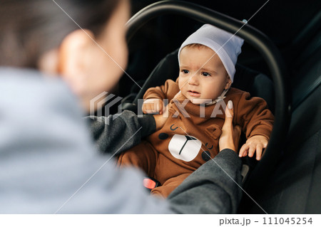 View from shoulder of unrecognizable young mother putting child safety seat with infant baby boy on back passenger seat. Concept of safety lifestyle, driving and travel. View from shoulder of unrecognizable young mother putting child safety seat with infant baby boy on back passenger seat. Concept of safety lifestyle, driving and travel. 111045254